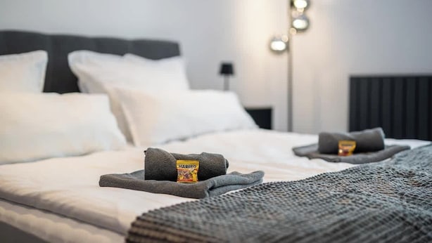 Una cama bien hecha con una manta gris y una barra de chocolate Haribo a un lado.