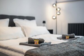 Un lit bien fait, avec une couverture grise et une barre chocolatée Haribo posée sur la table de chevet.