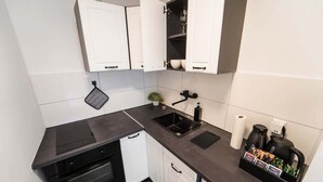 A compact kitchen with white cabinets, a black countertop, a built-in oven, a sink, and a coffee maker. - Exklusive 1-Zimmer Stadtwohnung in Bremen (Bremen)