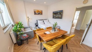 Une chambre moderne avec une table à manger en bois, des chaises jaunes, un canapé gris, un lit et une plante en pot.
