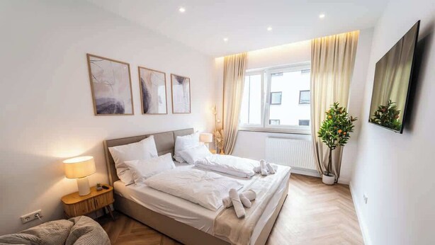 Une chambre d’hôtel moderne avec un grand lit, des tables de chevet, un canapé et une plante en pot.