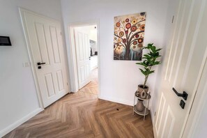 Ein Korridor mit Fischgrätparkett, einer weißen Tür, einem Baumgemälde und einem Blumentopf.