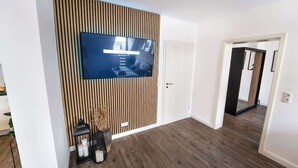 Ett modernt vardagsrum med en platt-TV som är monterad på en väggpanel av trä, en dörr och en hall som leder till ett annat rum.