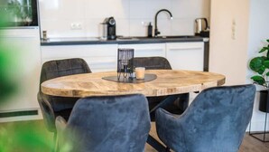 Ett runt träbord med en svart metallhållare för ljus och ett ljus, omgivet av två mörka stolar.