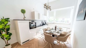 Una cucina moderna con mobili bianchi, un'area pranzo con sedie color beige e un'ampia finestra che offre luce naturale.