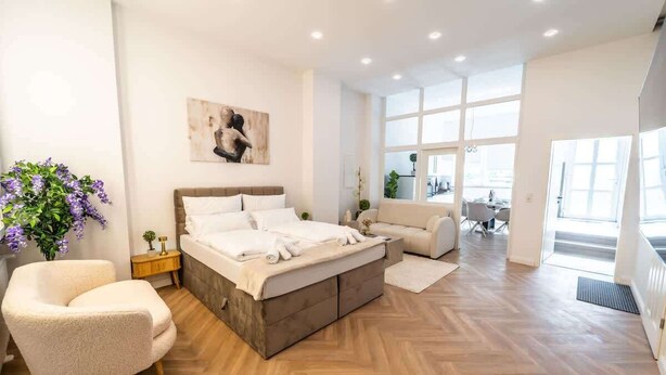 Una camera da letto moderna con un letto grande, una poltrona e una sedia. Si vede una finestra con vista all'esterno.
