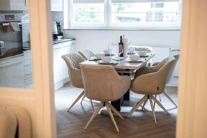 Eine moderne Küche mit Essbereich, ausgestattet mit einem für vier Personen gedeckten Tisch, Stühlen, einer Weinflasche und einer Kaffeemaschine.