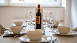 Un tavolo da pranzo apparecchiato con ciotole bianche, bicchieri da vino e una bottiglia.