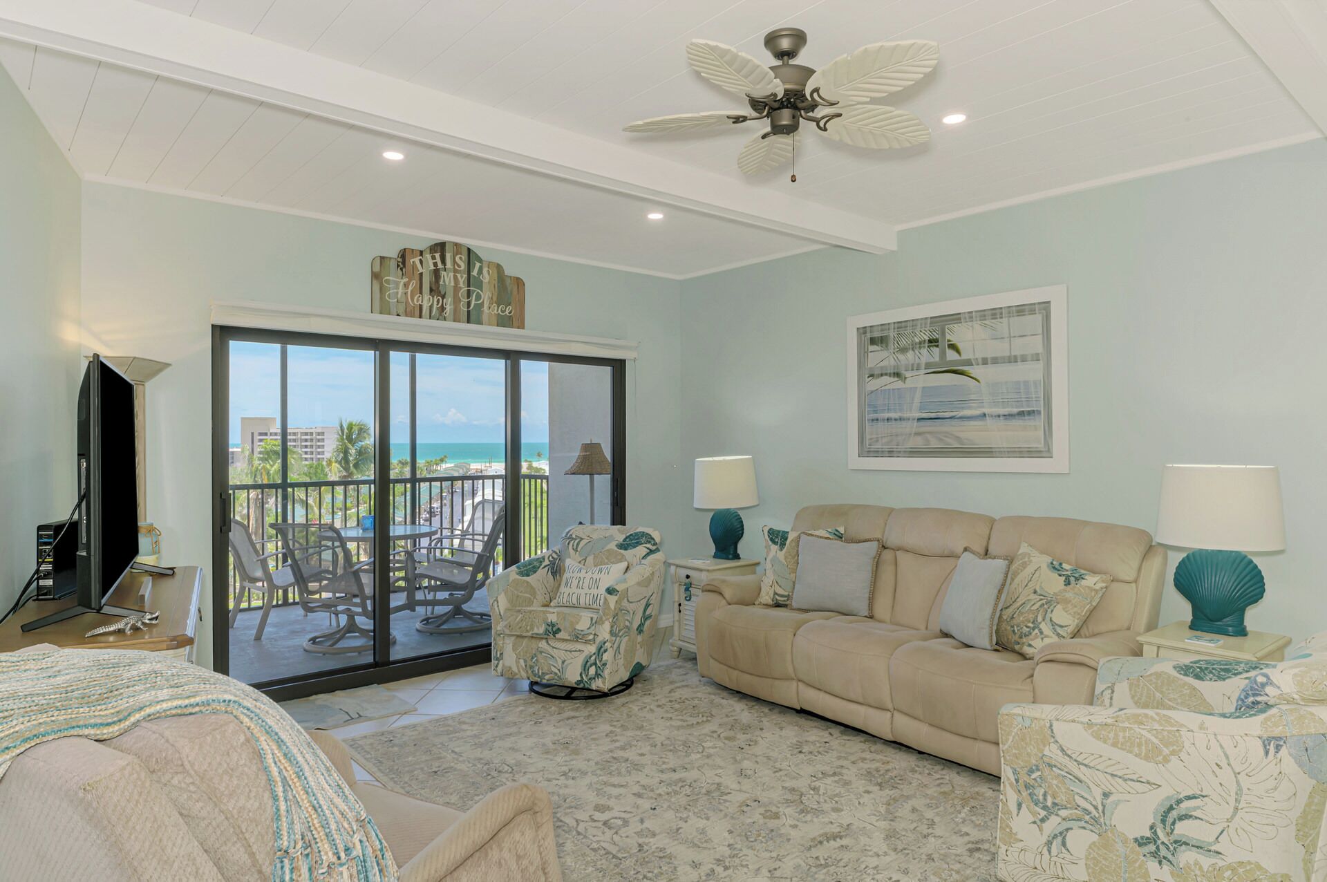 A spacious living room with a balcony, a ceiling fan, and a view of the ocean.