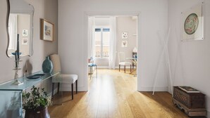 Een moderne woonkamer met een glazen salontafel, een witte bank en een houten vloer. Er is een deur die leidt naar een andere kamer met een balkon.
