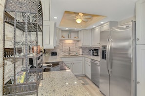 A modern kitchen with stainless steel appliances, white cabinetry, and a granite countertop. - Harbor Towers 605 - Tropical Sands Accommodations (Siesta Key)