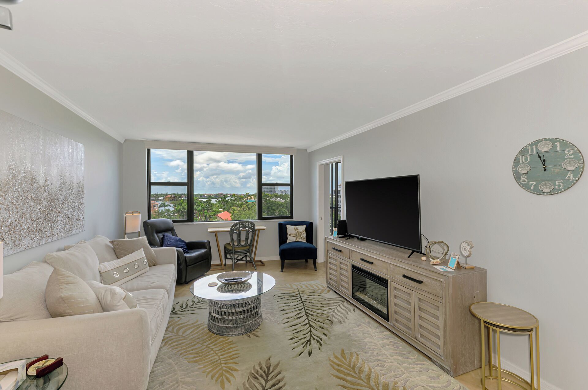 A modern living room with a large window, a flat-screen TV, a fireplace, and a decorative clock on the wall.