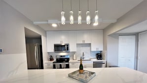Una cocina moderna con armarios blancos, una isla grande, electrodomésticos de acero inoxidable e iluminación colgante.