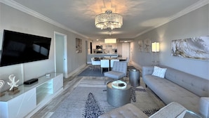 Una sala moderna con televisión de pantalla plana, candelabro, sofá y zona de comedor con sillas y una mesa.