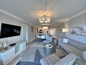 Ein modernes Wohnzimmer mit Flachbildfernseher, einer Chandelierleuchte, einer Couch und einem Essbereich mit Stühlen und einem Tisch.