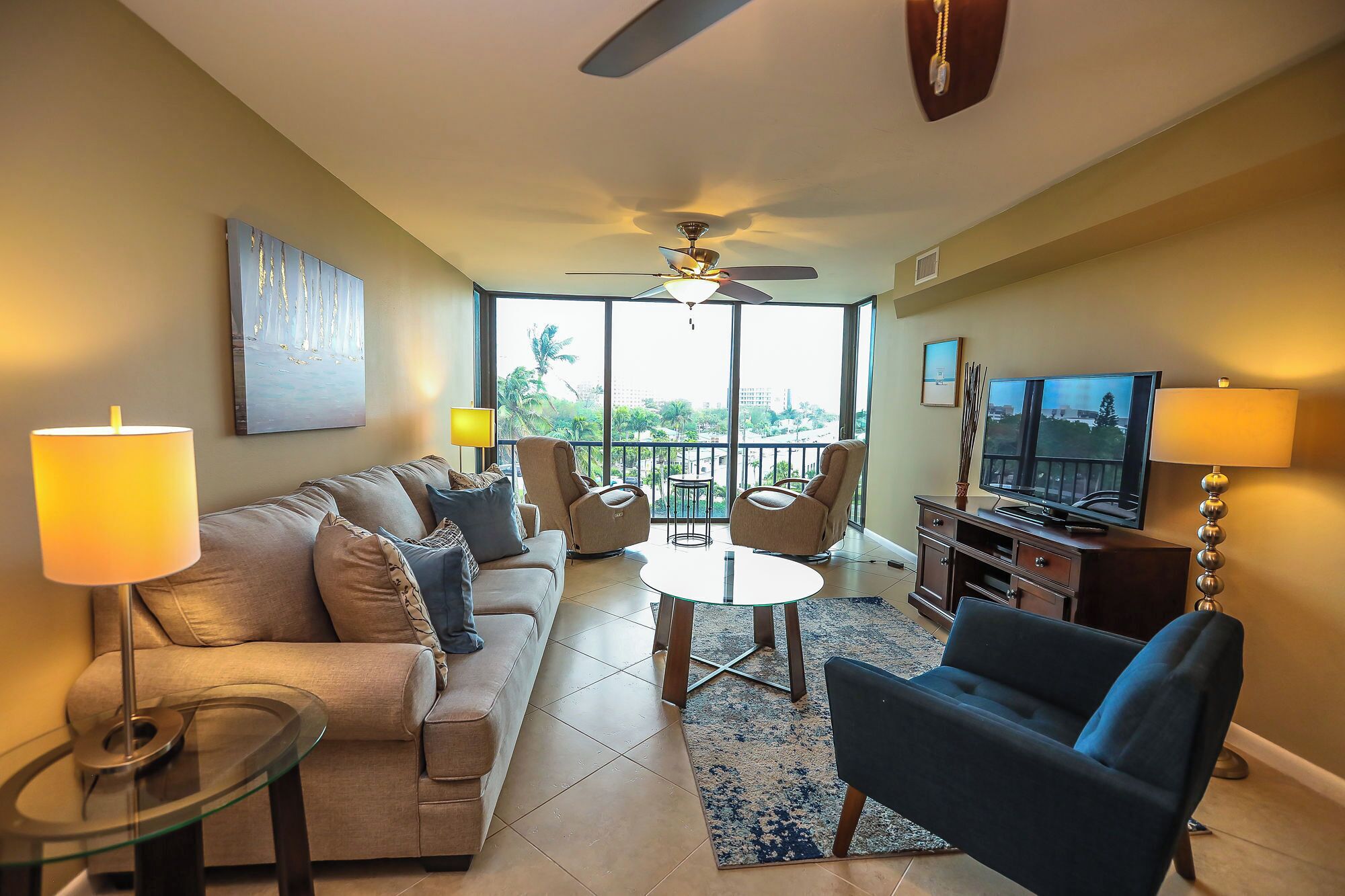 A living room with a sofa, chairs, a coffee table, a TV, and a ceiling fan.
