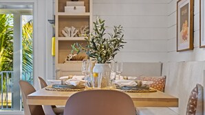 A dining area with a wooden table set for two, a vase with greenery, and a bookshelf in the background. - Luxury Family Getaway w/ Pool, Putting and Backyard Fun (Anna Maria)