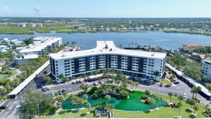 A large hotel with multiple floors, a parking lot, and a green landscaped area with a small pond. - Harbor Towers 326 - Tropical Sands Accommodations (Siesta Key)