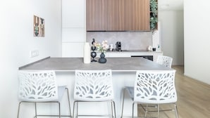 Een moderne keuken met witte kasten, een centraal eiland met barstoelen en een hanglamp.