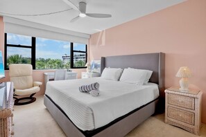 Un dormitorio con una cama grande, un ventilador de techo, un escritorio con una silla y una mesita de noche con una lámpara.