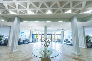 A spacious lobby with a glass table centerpiece, large windows, and a modern ceiling design. - Harbor Towers 303 - Tropical Sands Accommodations (Siesta Key)
