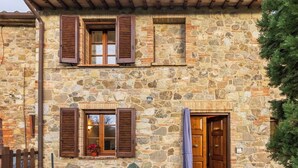 A stone building with wooden shutters and a wooden door. - CASA VECCIANO essence of Tuscany (Toscana)