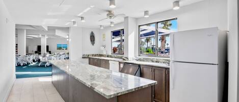 A modern kitchen with a marble countertop, dark wooden cabinets, and a white refrigerator.