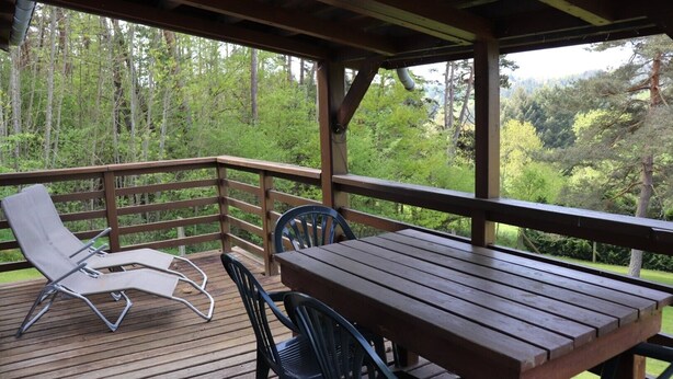 Eine Holzterrasse mit Tisch und Stühlen mit Blick auf eine bewaldete Landschaft.