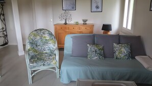 Ein Wohnzimmer mit einer Couch, einem Sessel, einer Holzkommode und zwei gerahmten Bildern an der Wand.