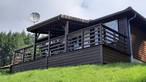 Eine Holzhütte mit Balkon, Satellitenschüssel und Blick auf den umliegenden Wald.