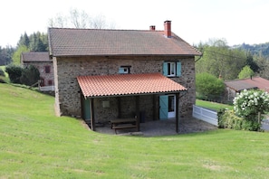 A stone house with a tiled roof, a covered porch, and a small window.