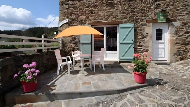 A stone building with a patio area featuring outdoor seating, a potted plant, and a window with shutters.