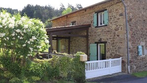 A stone building with a covered porch, a white fence, and a flowering tree.
