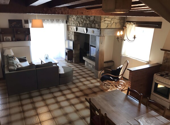 A cozy living area with a sofa, a dining table, a fireplace, and a television. - Beautiful Cottage in the Heart of Auvergne (Chassignolles)