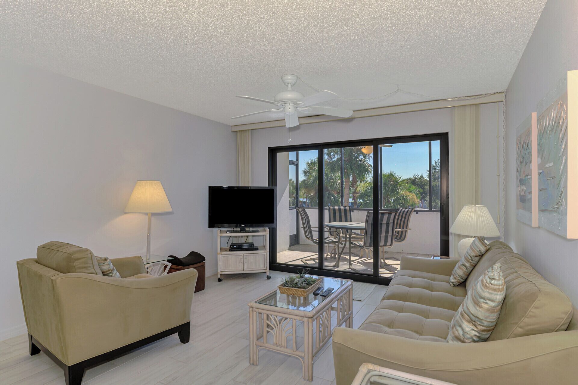 A spacious living room with a ceiling fan, a flat-screen TV, a sofa, a coffee table, and a dining area with chairs and a table.