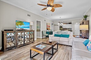A living room with a TV, wooden cabinet, white sofa, and a ceiling fan. - Harbor Towers 128 - Tropical Sands Accommodations (Siesta Key)