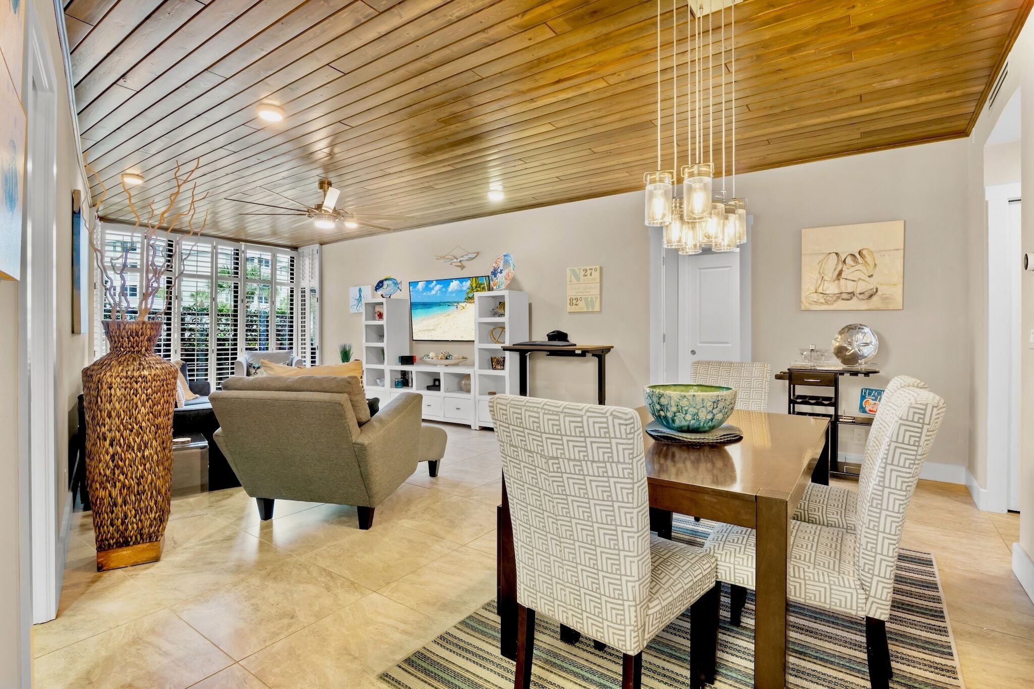 A spacious living area with a wooden ceiling, a large window, a dining table with chairs, and a television.