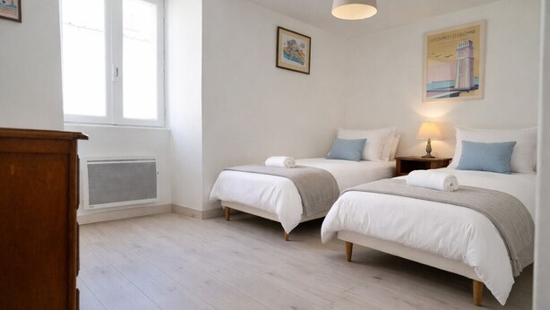 Une chambre avec deux lits, une fenêtre, un radiateur et une lampe.