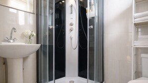 Une salle de bain moderne avec une douche à parois de verre, un lavabo agrémenté d’un vase de fleurs et un mur recouvert de carreaux blancs.