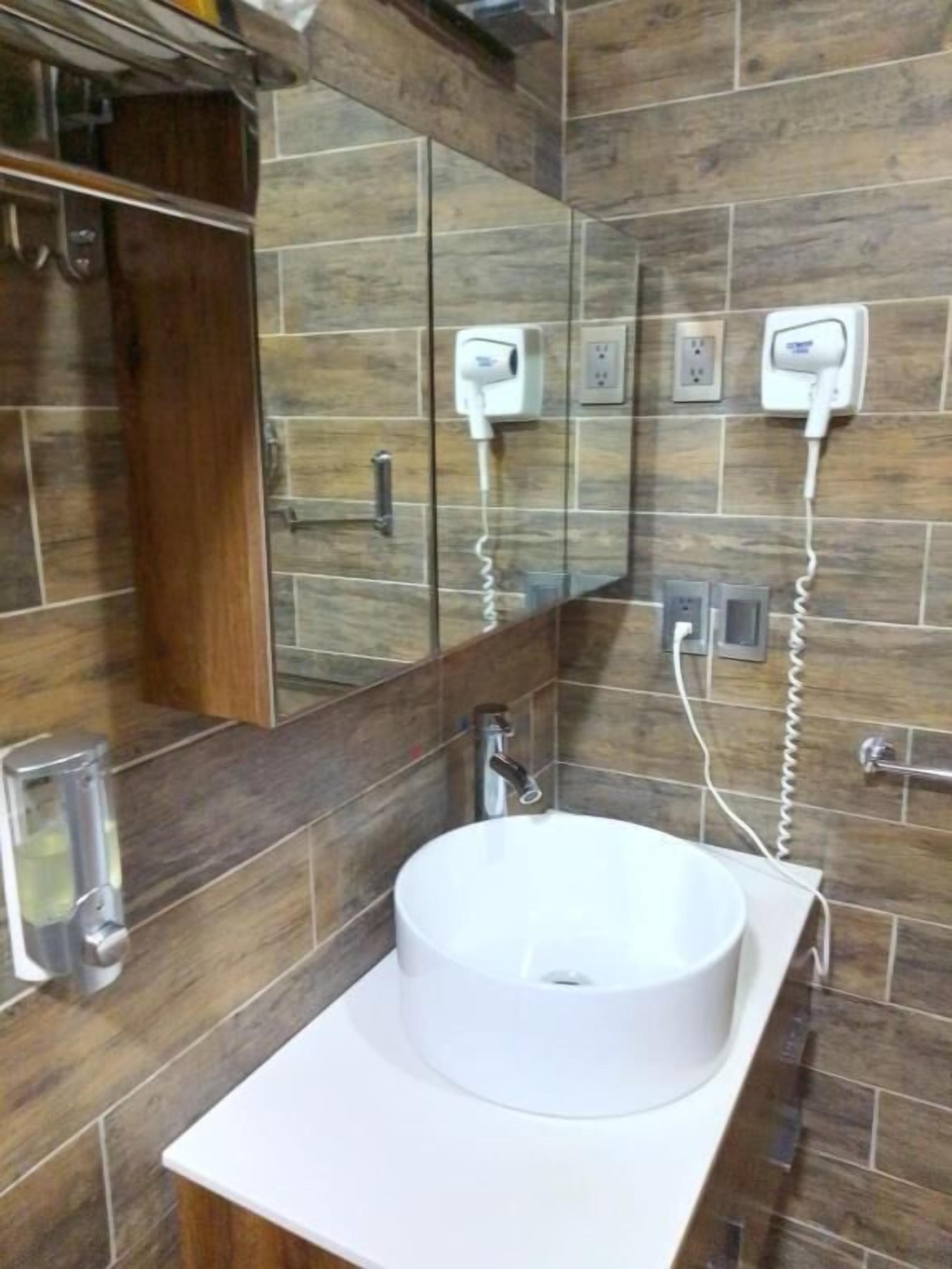 Um banheiro com uma pia branca, um espelho e dois secadores de cabelo fixados na parede.