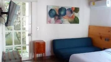 A room with a wooden ceiling, a bed, a blue sofa, a small wooden stool, a painting, and a suitcase.