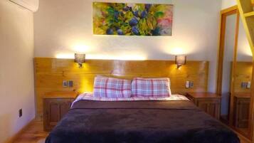 Una cama con estructura de madera, dos lámparas de noche, un cuadro en la pared superior y un armario de madera a la derecha.