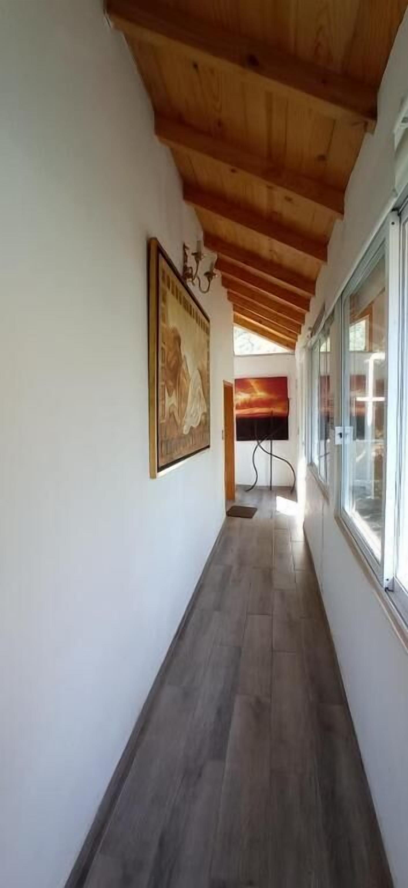 A hallway with wooden ceiling beams, a framed picture on the wall, and a window on the right.