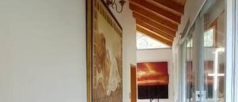 A hallway with wooden ceiling beams, a framed picture on the wall, and a window on the right.