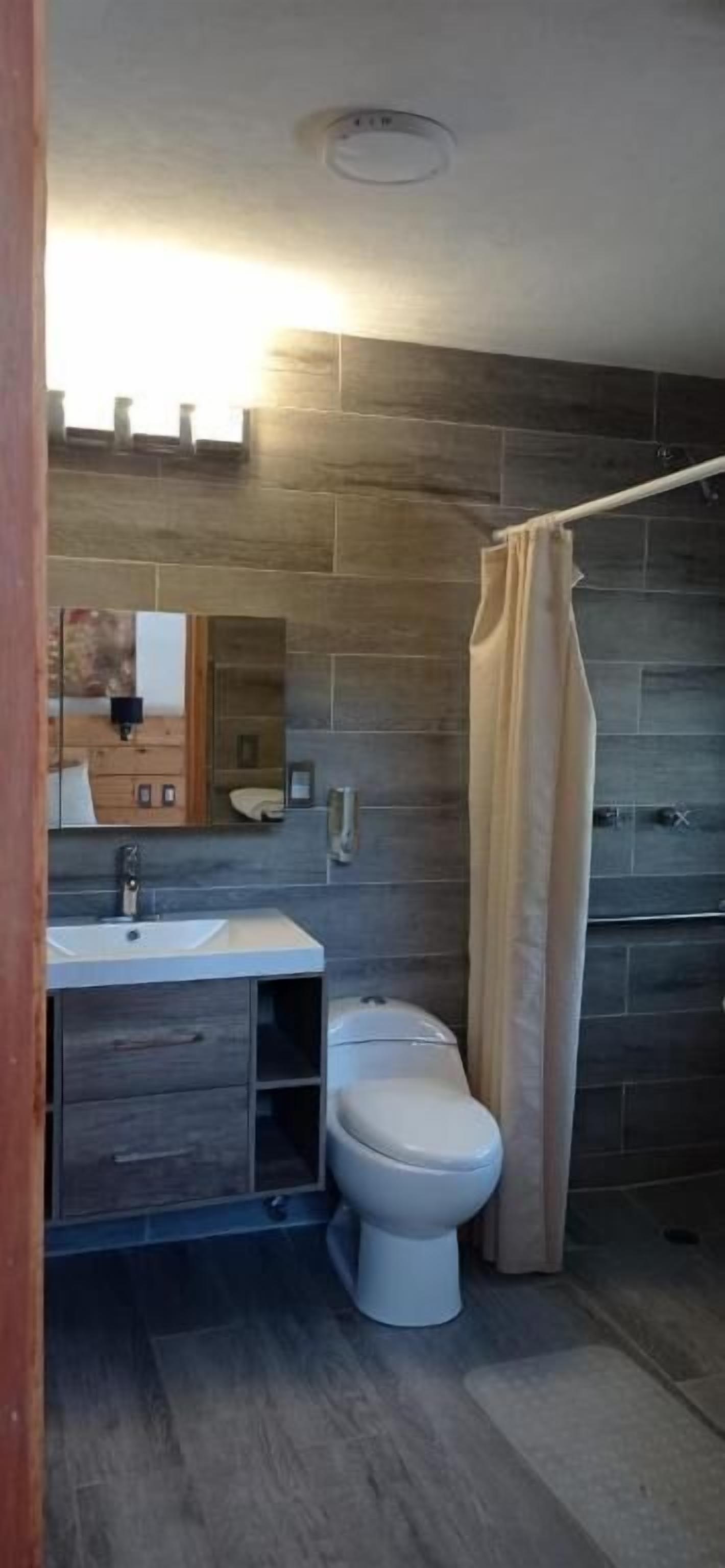 A bathroom with a modern design, featuring a stone wall, a white sink, and a toilet.