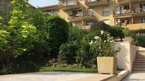 Un immeuble résidentiel à plusieurs étages, doté de balcons, d’un chemin pavé et entouré de verdure.