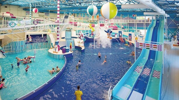 En inomhusbadpark med flera vattenrutschkanor, pooler och en stor, central vattenattraktion.