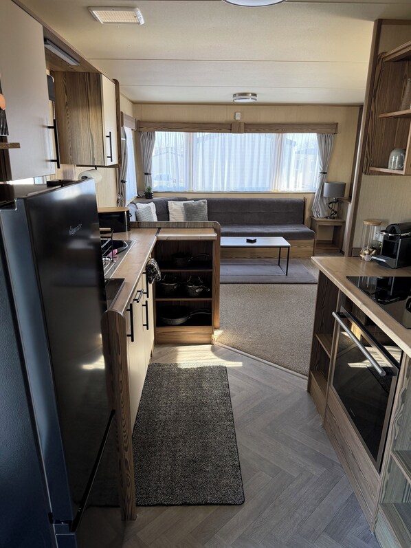 Een kleine keuken met een ingebouwde oven, een koelkast en een zithoek met een bank en een tafel.