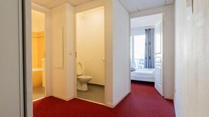 Een hotelkamer met een rood tapijt, een badkamer met toilet en wastafel, en een balkon met uitzicht.