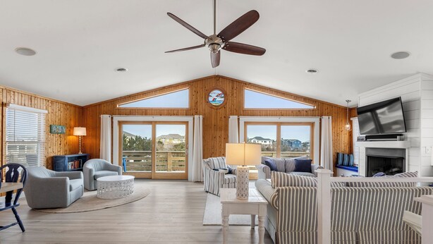 A spacious living room with a high ceiling fan, large windows, and a fireplace. - Tails in the Sand: Private Heated Pool | Hot Tub | Dogs OK (Corolla)